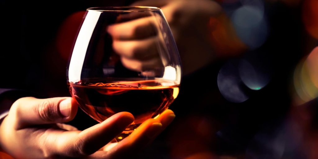 A close-up of a hand elegantly holding a snifter glass filled with amber-coloured cognac. 