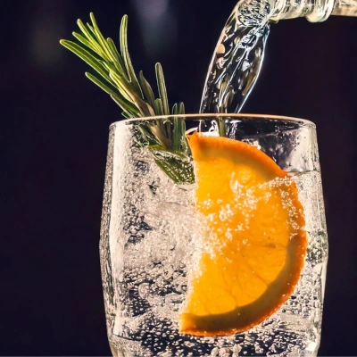 Close-up of a classic gin and tonic being poured into a glass with orange and rosemary