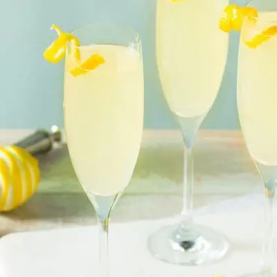 Three sparkly French 75 cocktails garnished with lemon twists , set against a blue backdrop