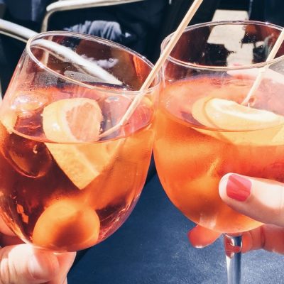 Two hands clinking Aperol Spritz together
