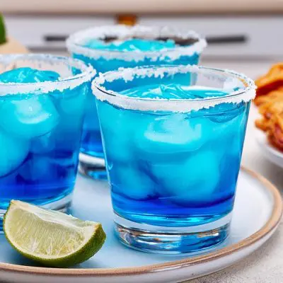 Three Blue Margarita cocktails served with empanadas in a kitchen setting