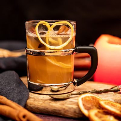 A mug of Apple Cider Hot Toddy on a wooden tray surrounded by fall decoration elements