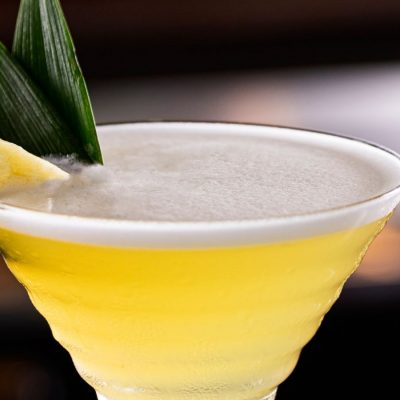 Extreme close up of a Pineapple Martini garnished with a fresh slice of pineapple, presented against a dark backdrop