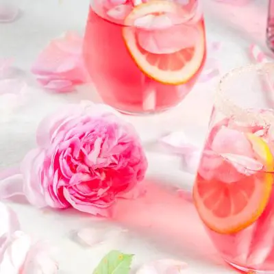 Three pretty pink Mother's Day cocktails arranged on a white backdrop with a pink rose and some petals scattered to add a little whimsy