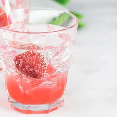 A pair of pretty pink-hued Shirley Temple cocktails garnished with cherries, standing on a white surface, one behind the other