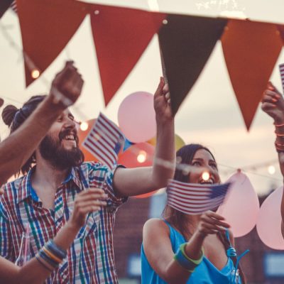 Close up of a group of friends waving small Americal flags and having a good time at dusk at a Memorial Day party