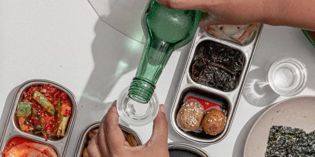 Close up top view of a person pouring a shot on a table set with popular Korean foods