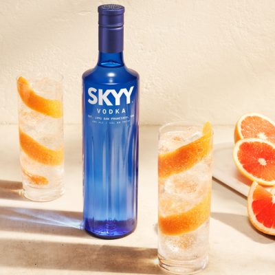Two SKYY Vodka Soda cocktails with grapefruit peel garnish and a bottle of SKYY Vodka