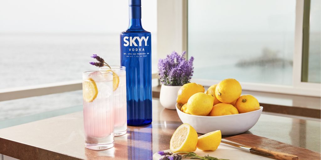 Two Sparkling Lavender Lemonade vodka cocktails with a bottle of SKYY, bowl of lemons and lavender on the table