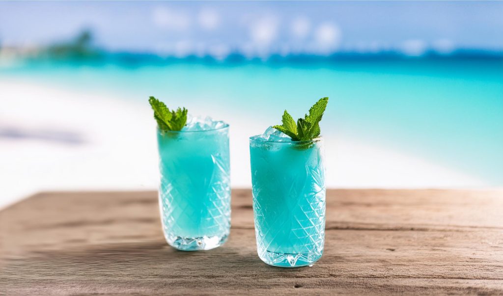 Two SKYY Vodka Market Street Mai Tai rainbow cocktails with mint garnish, on a wooden table with a scenic beach in the background 