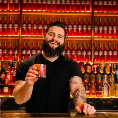 A mixologist holding a cocktail while standing behind the bar