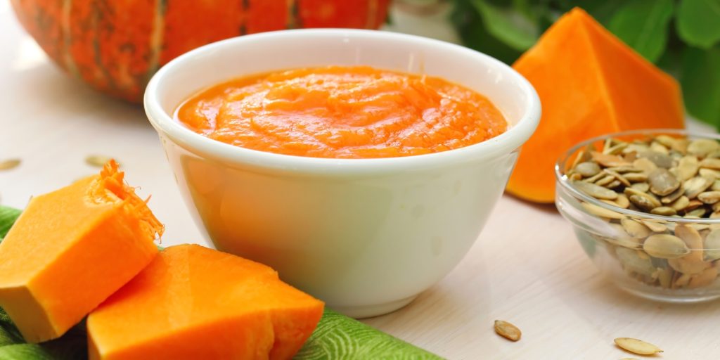 Close up of a bowl of pumpkin puree in a home kitchen next to fresh slices of pumpkin