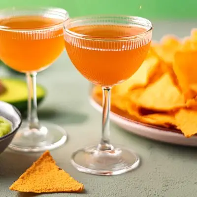 Two Naked and Famous Cinco de Mayo cocktails served with nachos and guacamole