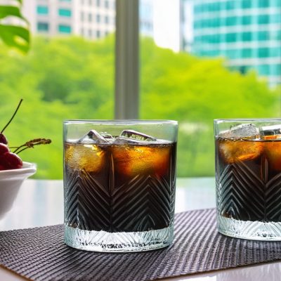 Two Black Russian cocktails served with a bowl of maraschino cherries, city backdrop through large windows in the background