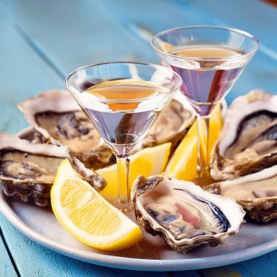 A plate of tiny vodka martini cocktails and fresh oysters with lemon wedges