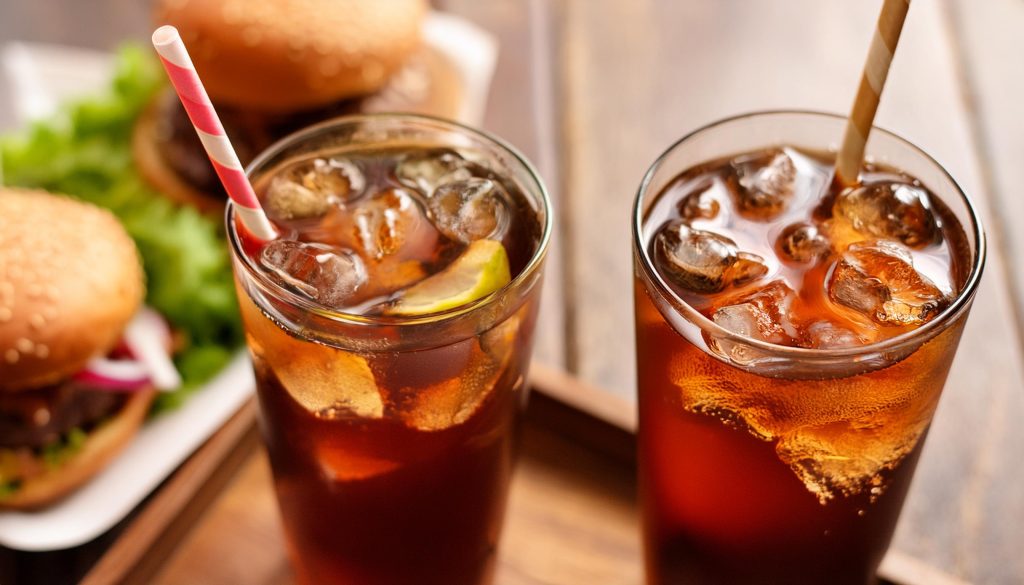 Two White Rum cocktails with cola in tall glasses next to a burger on a wooden table