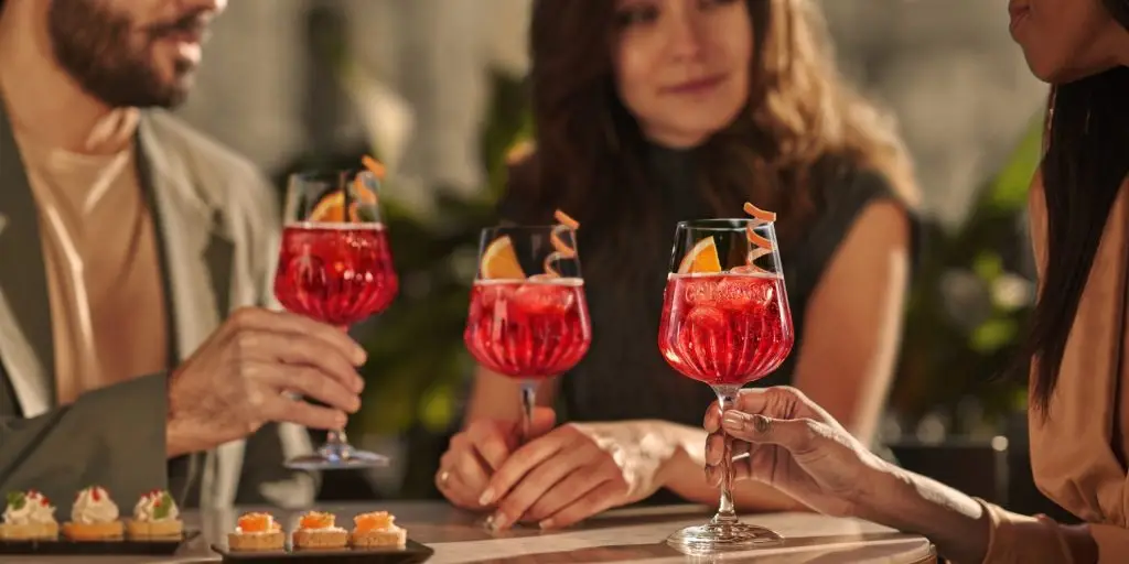 Close-up of three Campari Spritz cocktails, people sitting at a table blurred out