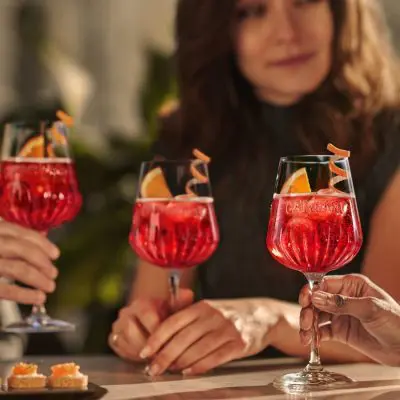 Close-up of three Campari Spritz cocktails, people sitting at a table blurred out