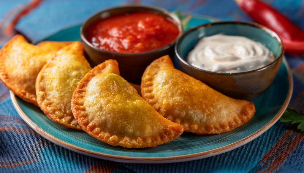 Crispy Empanadas on a blue plate served with bowls of tomato salsa and sour cream