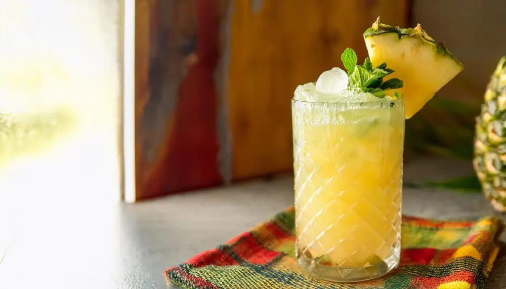 A Pineapple Margarita served in a tall glass with mint and pineapple garnish