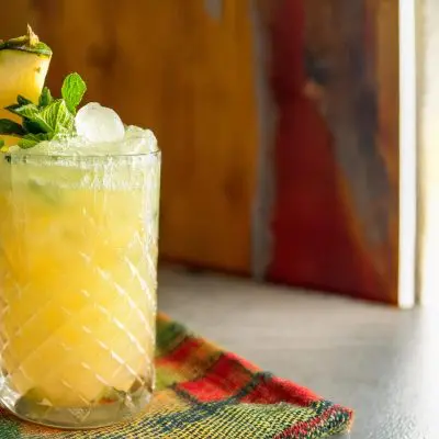 A Pineapple Margarita served in a tall glass with mint and pineapple garnish