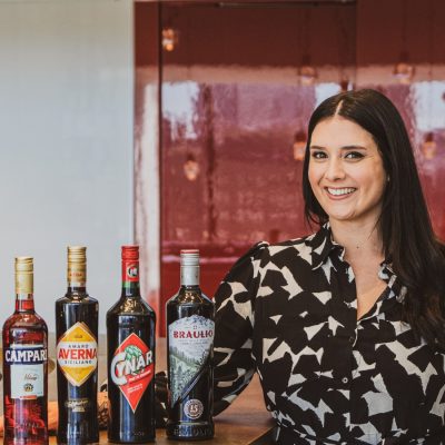 Campari Brand Ambassador Oliva Cerio posing next to a bar counter, red staircase in background