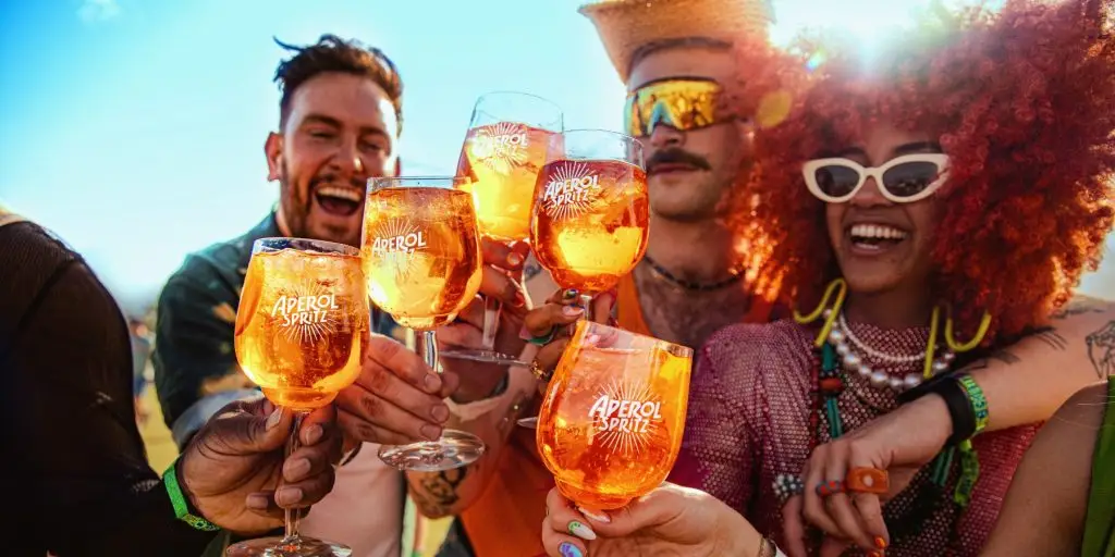 Close-up of friends outdoors in the sunshine clinking together their vibrant orange Aperol Spritz cocktails