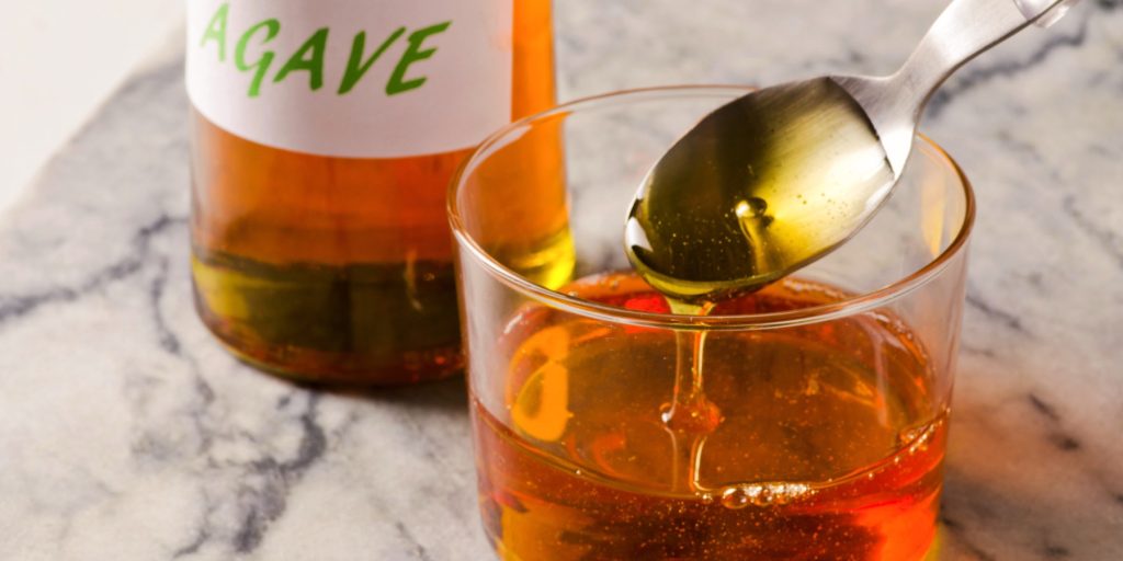 Close up of agave syrup in a clear bowl next to a bottle of agave syrup