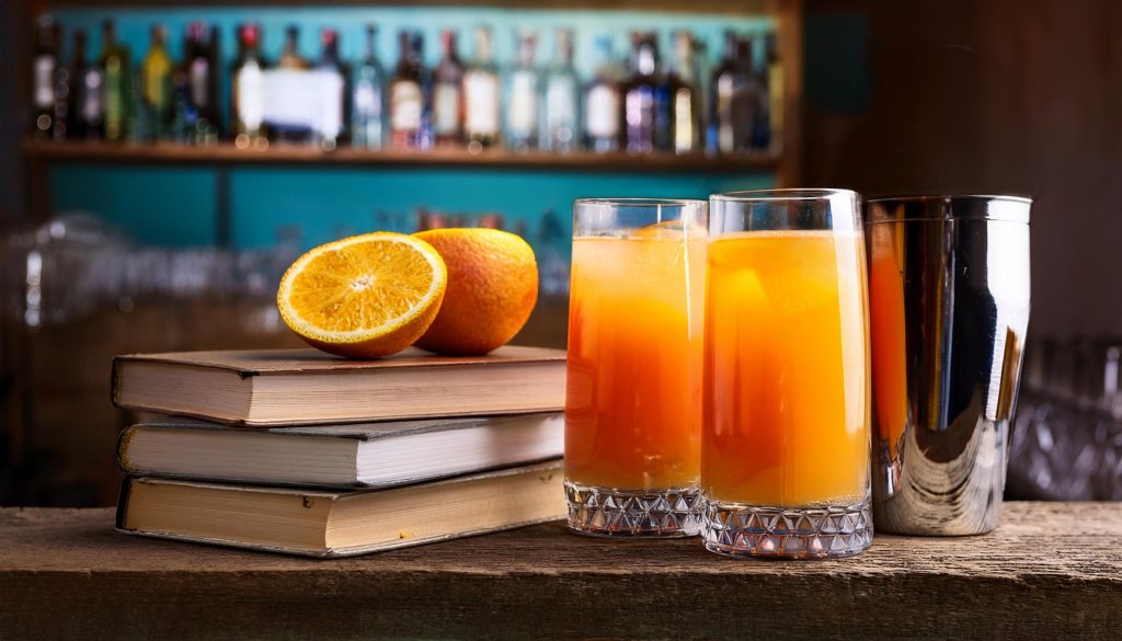 Close up of two tequila and orange juice cocktails on a table in a home kitchen next to a stack of recipe books