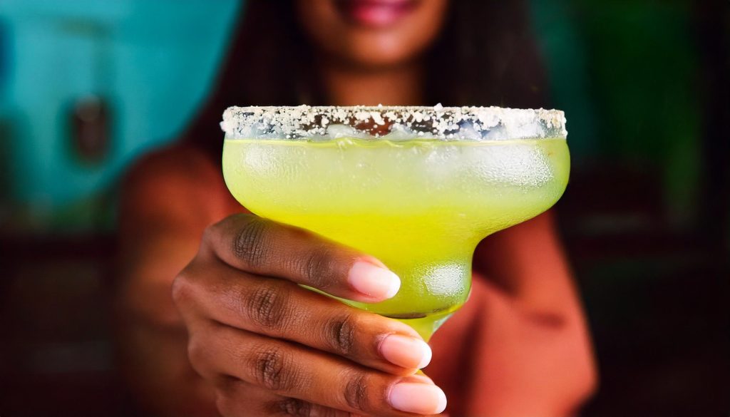 Close-up of a hand holding a Lime Margarita with salted rim