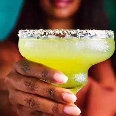 Close-up of a hand holding a Lime Margarita with salted rim