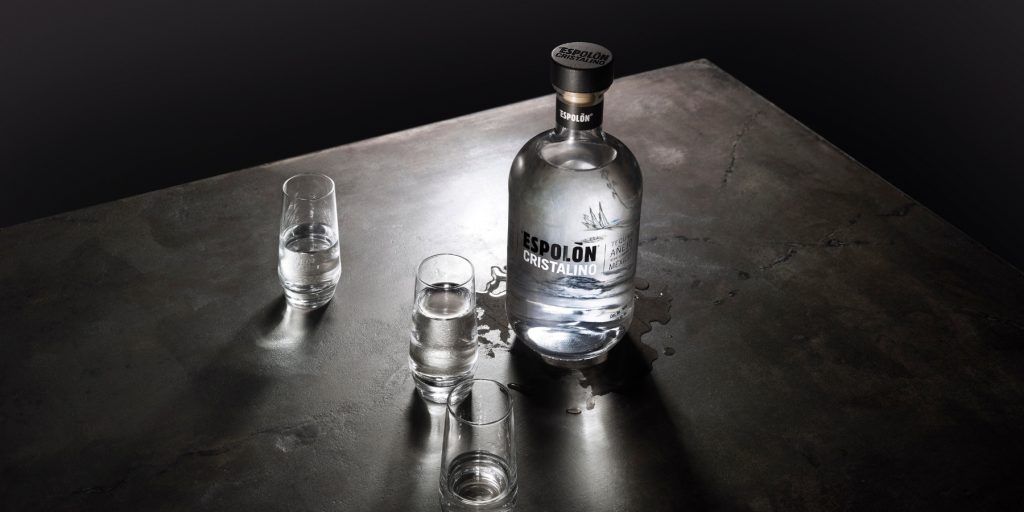 A slightly overhead and moody shot of a bottle of Espolòn Cristalino tequila and two shot glasses