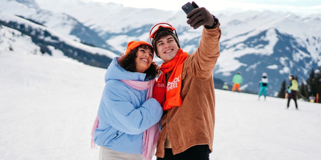 A couple on mountain slopes in winter outfits taking a selfie